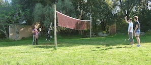 An outdoor area with a volleyball net, trees, and a picnic table.