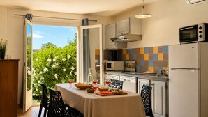 Une cuisine équipée d’une table à manger, d’un four à micro-ondes et d’un réfrigérateur, avec vue sur la verdure environnante.