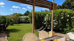 Une terrasse agrémentée d’une pergola, avec des sièges d’extérieur et une table préparée pour deux personnes, avec des boissons.