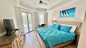 Una camera da letto con un letto, una TV, una scrivania e una ventola a soffitto.