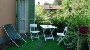 Un balcón al aire libre con césped verde, sillas blancas y una pequeña mesa.