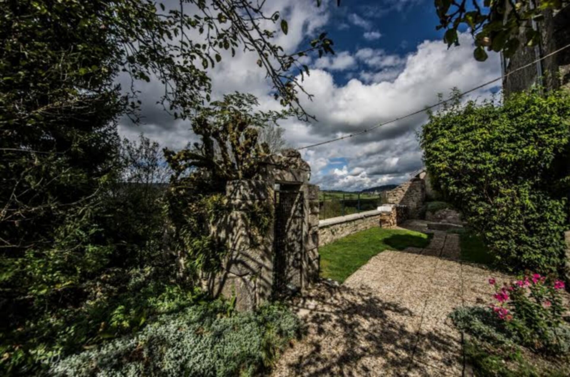 A stone pathway leading to a stone wall, surrounded by lush greenery and flowering plants.