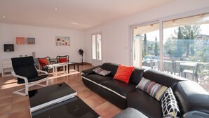Un salon moderne avec un canapé en cuir noir, une table basse blanche et un coin repas comprenant une table et des chaises blanches.