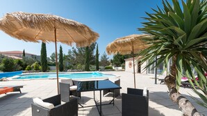 Un espace aménagé au bord de la piscine, avec deux parasols en chaume, des meubles en osier et une piscine.