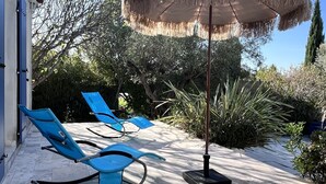 Une terrasse avec des chaises longues bleues et un parasol en chaume.