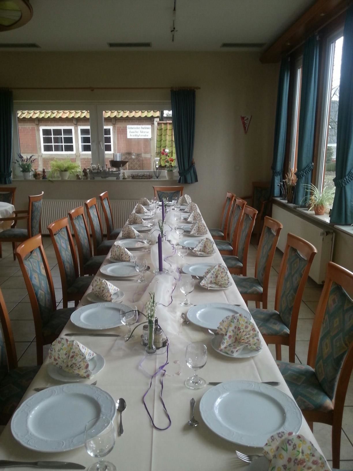A long dining table set for a meal with chairs on both sides, a view of the outside through windows, and a brick wall in the background.