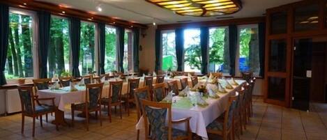 Un salón de conferencias con varias mesas y sillas, ventanas amplias con cortinas y un candelabro en el techo.
