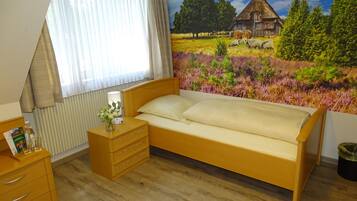 Un dormitorio con una cama de madera, una mesita de noche con lámpara, un aparador y una ventana con cortinas.