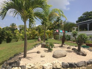 Stroll through a serene garden oasis with lush tropical plants, a small pond, and a covered patio area.