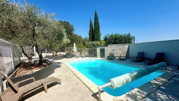 A rectangular swimming pool with a clear blue water surface, surrounded by a tiled patio area. There are lounge chairs and a covered seating area along the poolside. - Large contemporary house with garden (Seillons-Source-d'Argens)