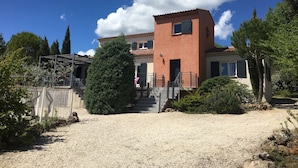 A two-story building with a red facade, a small tower-like structure, and a gravel driveway leading to a set of stairs. - Large contemporary house with garden (Seillons-Source-d'Argens)