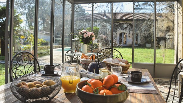 Una mesa de desayuno con un bol de naranjas, una jarra de jugo de naranja y una cesta de pan.