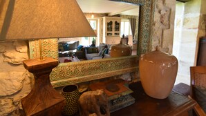 Une pièce dotée d’un grand miroir qui reflète un espace de vie, d’une table en bois avec une lampe et d’un grand vase.