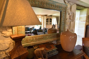 Una habitación con un espejo grande que refleja una sala de estar, una mesa de madera con una lámpara y un jarrón grande.