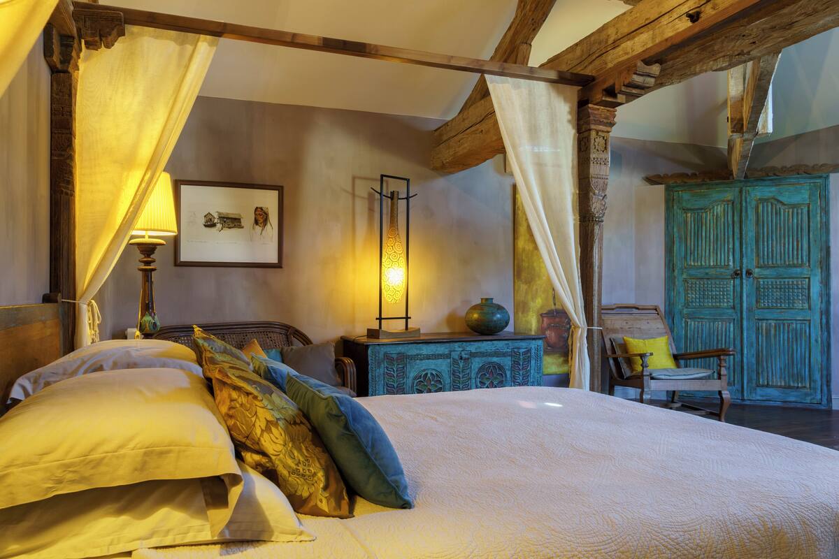 Un dormitorio tradicional con cama con dosel, una mesita de noche, una lámpara y un armario de madera.