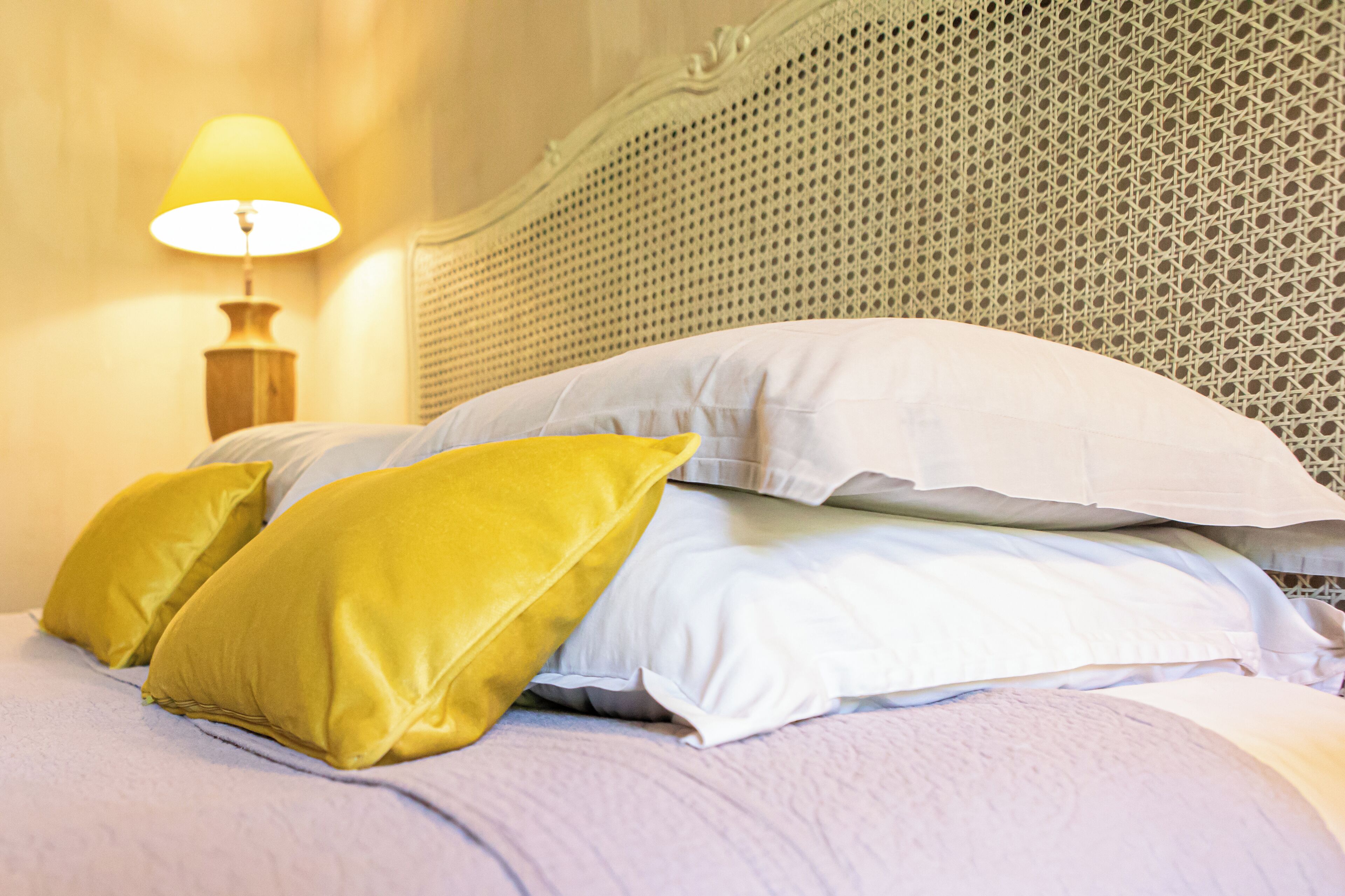 A bed with white and yellow pillows, a wooden nightstand with a lamp, and a textured headboard.