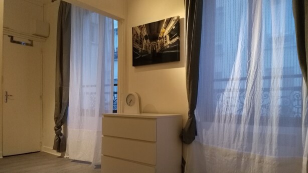 A room with a wooden floor, a white dresser, a clock, and a painting of a train. - Comfy Parisian studio! (Ivry-sur-Seine)