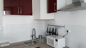 A kitchen with white tiled backsplash, a stainless steel sink, a microwave, and hanging kitchen utensils. - Comfy Parisian studio! (Ivry-sur-Seine)