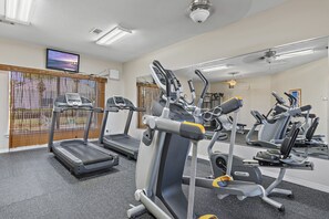 Et fitnessrum med løbebånd, crosstrainere og et fjernsyn på væggen.