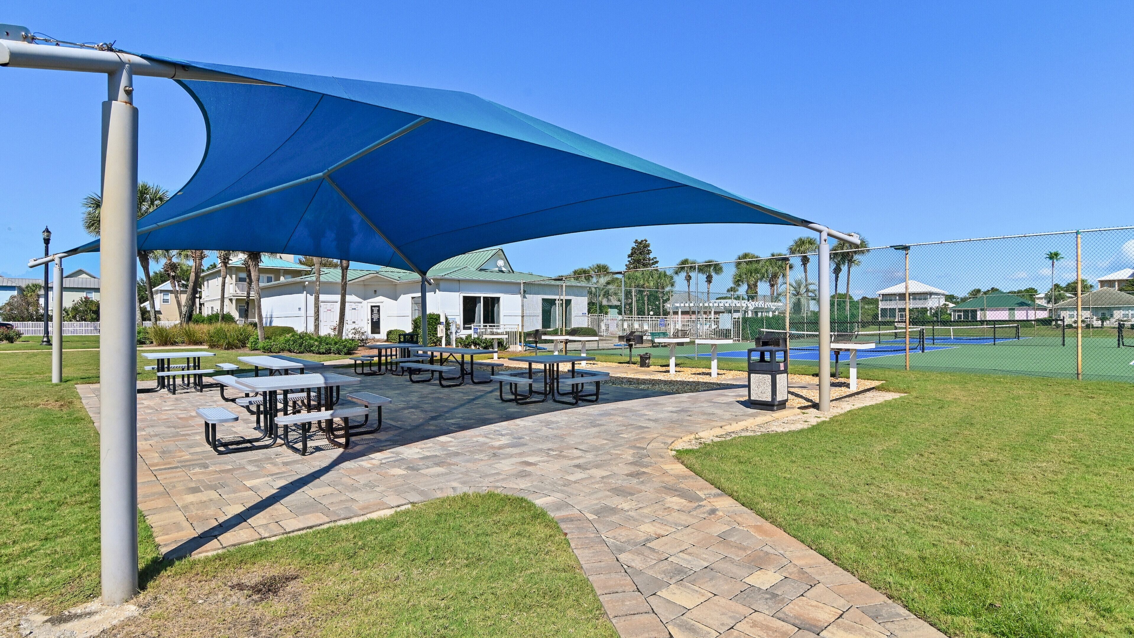 A patio area with picnic tables, a blue canopy, and a tennis court.