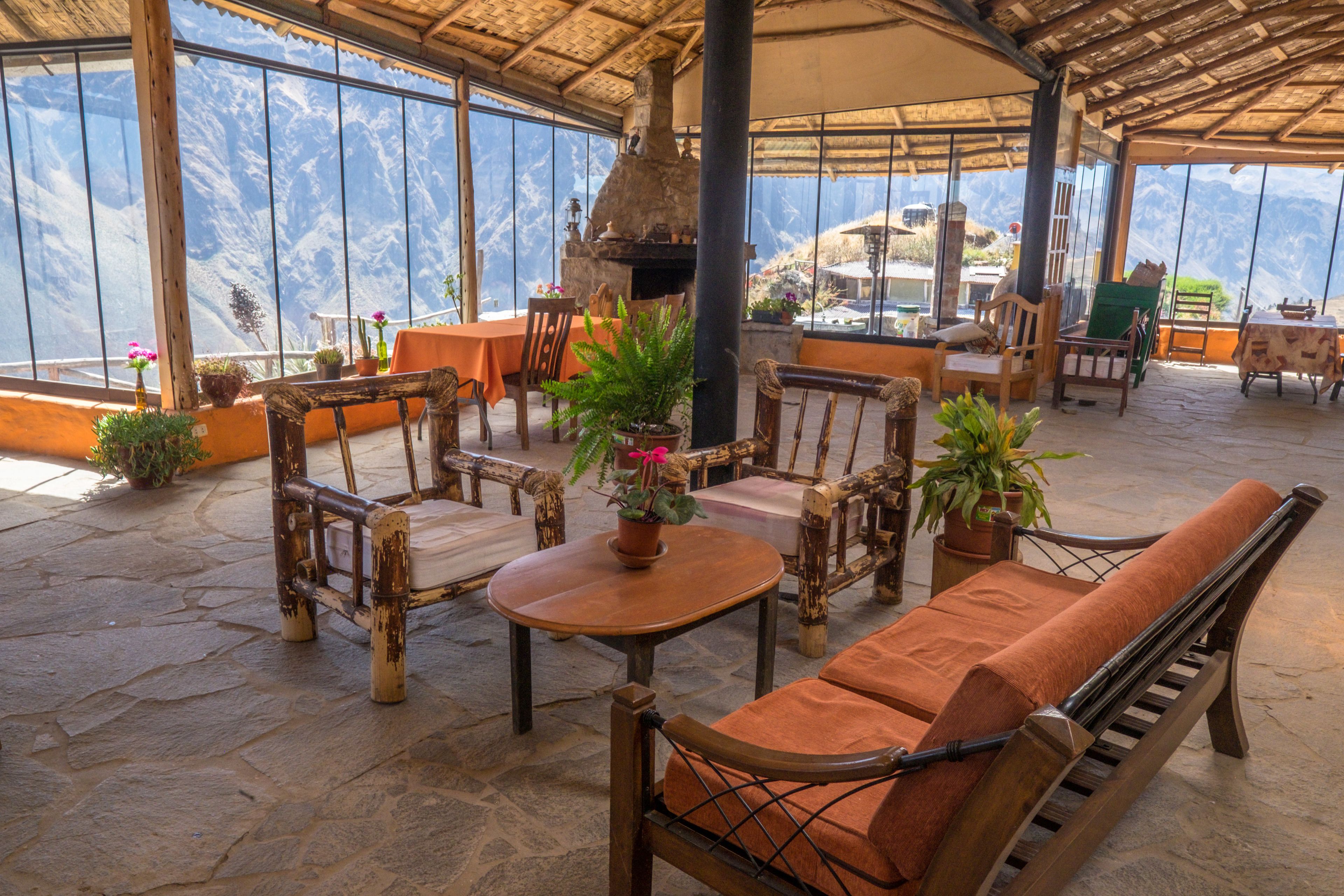 An outdoor seating area with rustic furniture, a stone floor, and large windows offering mountain views.
