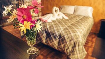 Una cama con un cojín en forma de corazón y un ramo de flores en un florero de vidrio sobre una mesa de madera.
