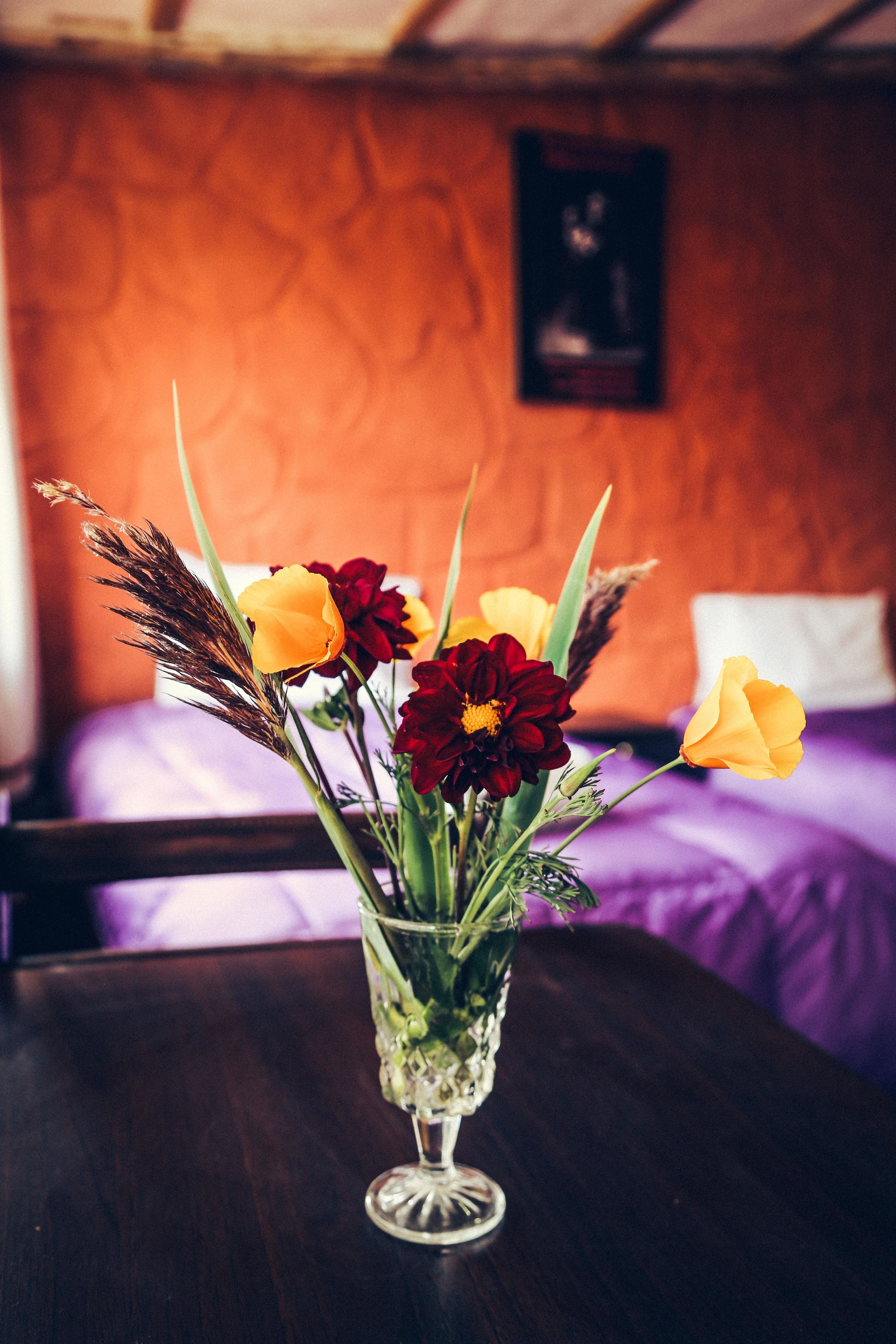 Eine Vase mit Blumen auf einem Tisch in einem Zimmer mit einem Bett und einem Poster an der Wand.