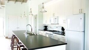 Una cocina moderna con una isla grande, armarios blancos, electrodomésticos de acero inoxidable e iluminación colgante.