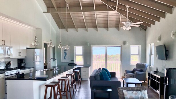 Cocina amplia con una isla central, taburetes de bar y un comedor con mesa de vidrio.