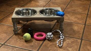 A pet feeding station with two bowls and a toy ball on a tiled floor.