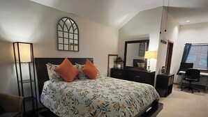 A bedroom with a large bed, a desk, a chair, a dresser, a mirror, and a floor lamp. - Work & Play in our High Country Hideaway (Boone)
