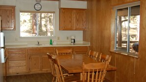 A kitchen with wooden cabinets, a dining table, chairs, a clock, a window, and a coffee maker.