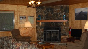 A cozy living room with a stone fireplace, wooden furniture, and a television.