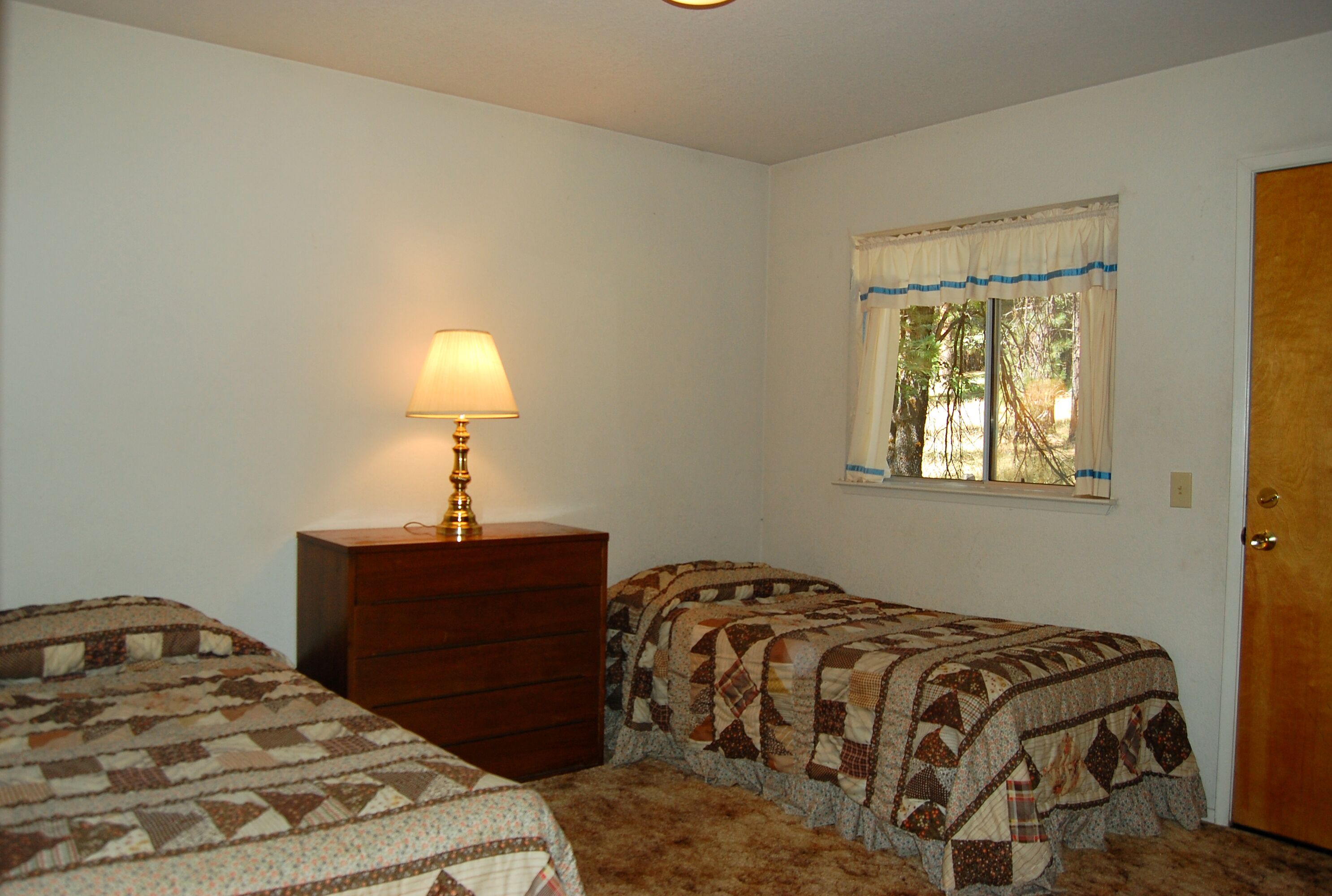 Un dormitorio con dos camas individuales, un tocador, una ventana con cortinas y una lámpara.