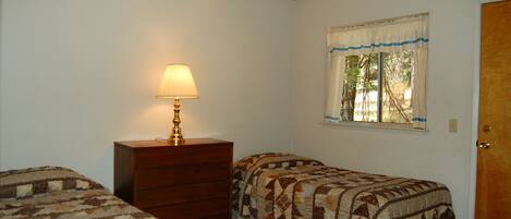Un dormitorio con dos camas individuales, un tocador, una ventana con cortinas y una lámpara.
