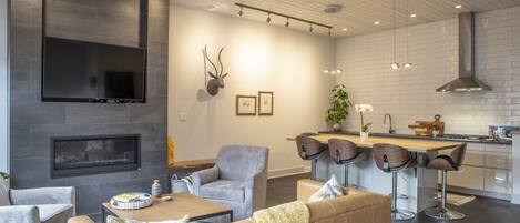 A modern living room with a fireplace, seating area, and a kitchen with bar stools.