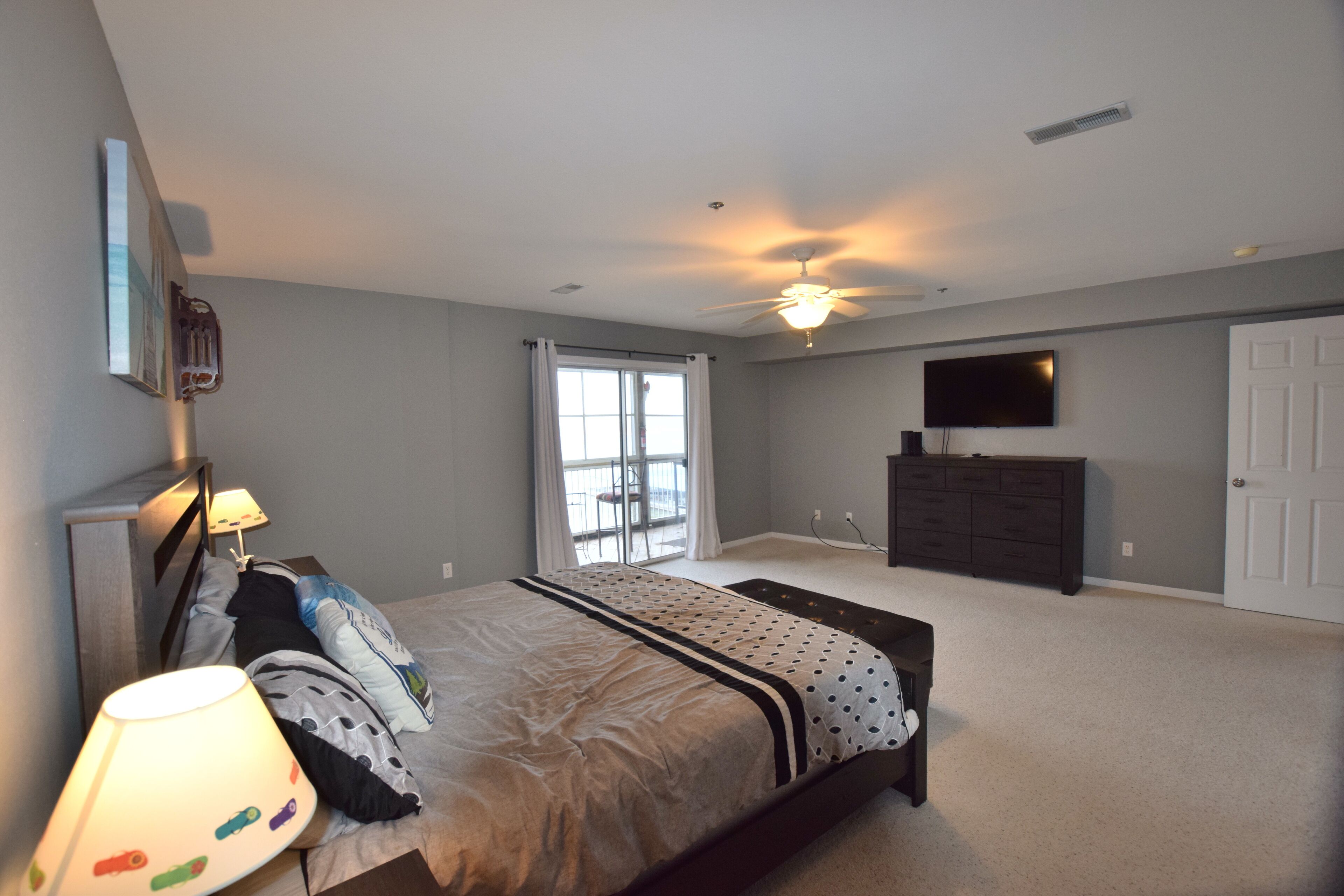 A bedroom with a bed, a dresser, a television, and a ceiling fan.