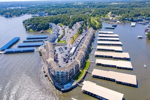 An aerial view of a waterfront property with a curved building, parking lots, and docked boats.