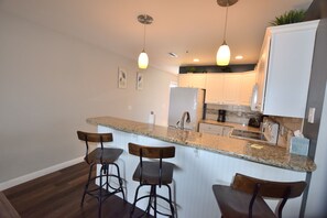 Una cocina con encimera de granito, armarios blancos y tres taburetes de bar.