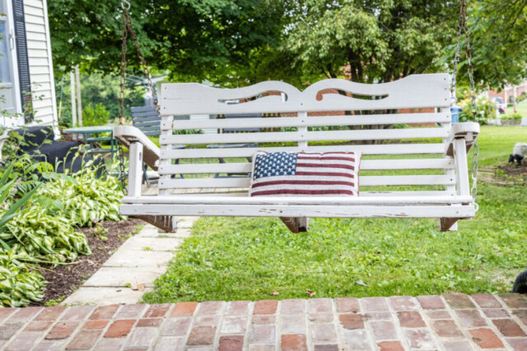 Eine weiße Bank mit Kopfkissen mit amerikanischer Flagge in einem Garten.