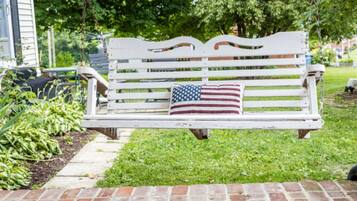 Eine weiße Bank mit Kopfkissen mit amerikanischer Flagge in einem Garten.