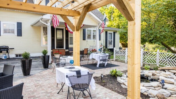 Un espace extérieur aménagé en terrasse, avec des tables et des chaises, une pergola et des drapeaux américains.
