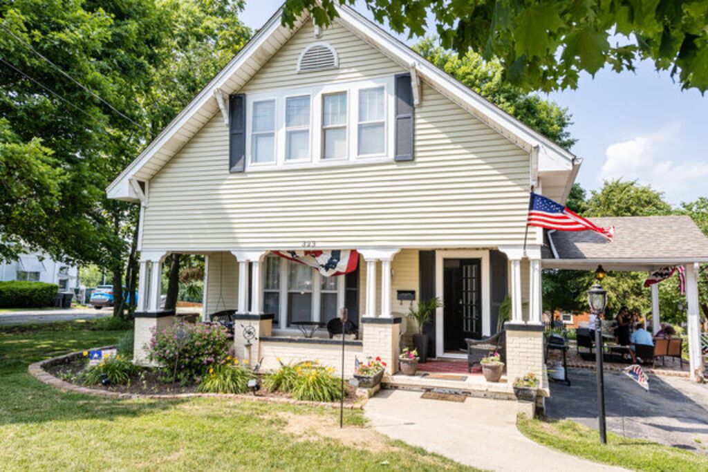 A two-story house with a porch, a small front yard, and an American flag.