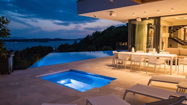 A modern outdoor pool area with a view of the sea, a dining area with a table and chairs, and a staircase leading to an upper level. - Beautiful professionally managed villa, walking distance to the Hvar City center (hvar)