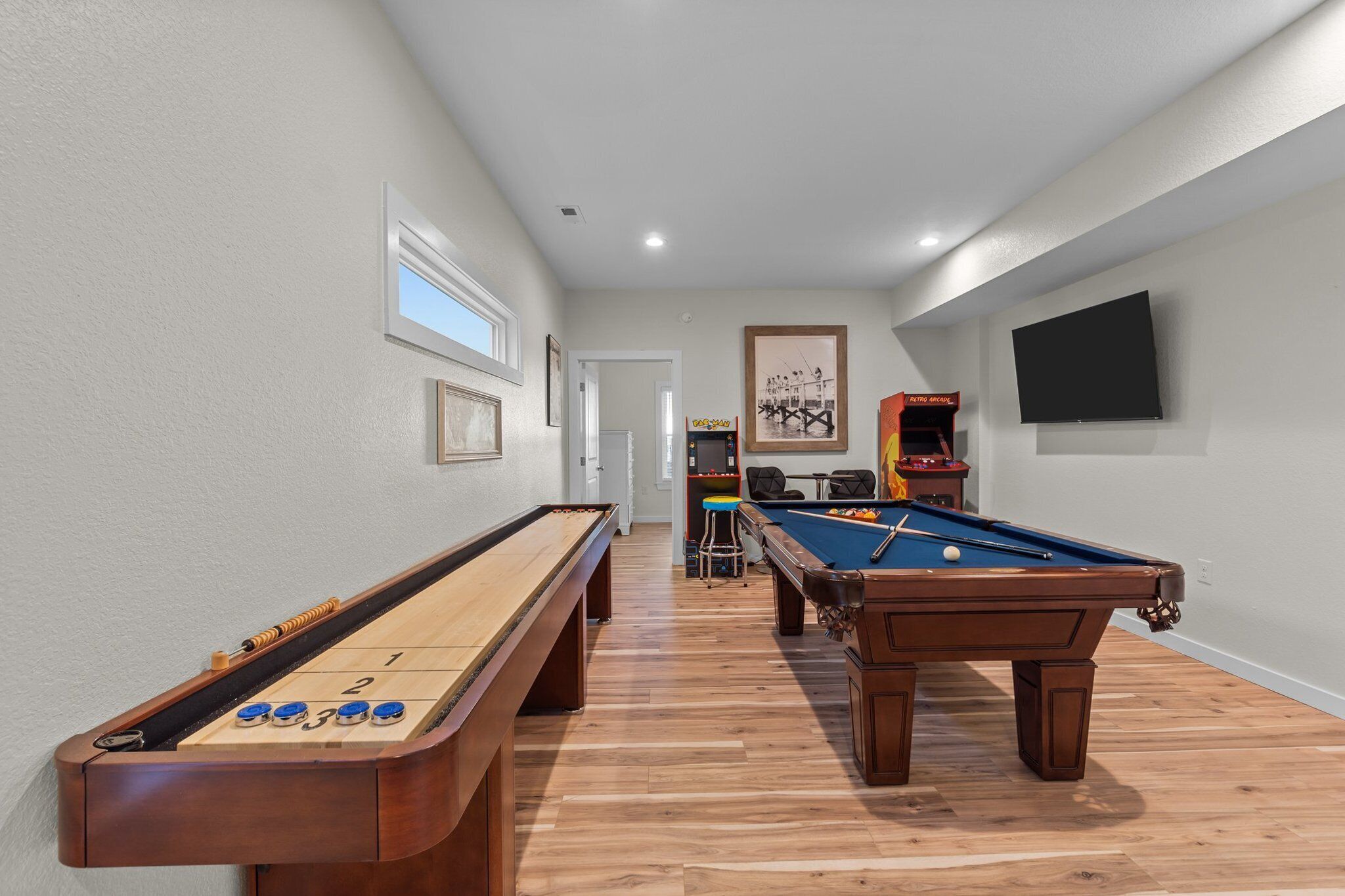 A pool table and shuffleboard table in a hallway with a TV on the wall.