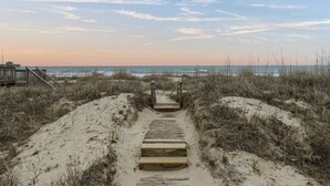 Un paseo marítimo de madera que lleva a una playa, con una estructura de madera a la izquierda.