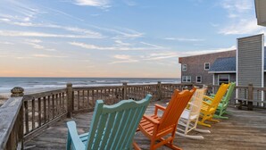 Terraza de madera con sillas Adirondack de colores con vistas a la playa.