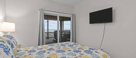 Ein Schlafzimmer mit Bett, einem an der Wand befestigten Fernseher und einem Balkon mit Meerblick.