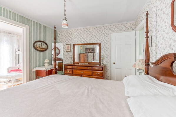 A bedroom with a large bed, a dresser with a mirror, and a chair.