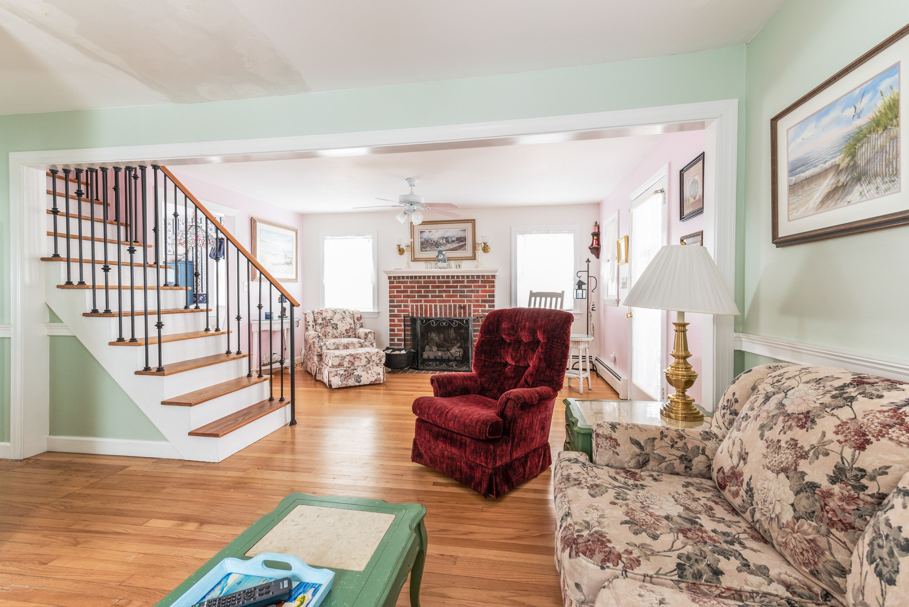 A spacious living room with a wooden staircase, a fireplace, and floral-patterned furniture.